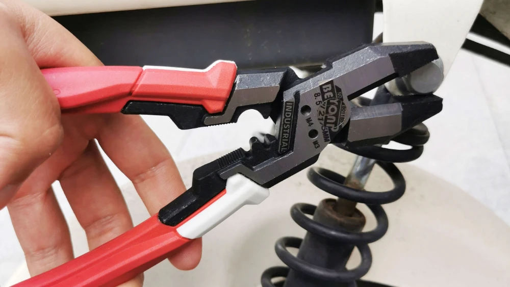 Red and white handle heavy duty plier twisting a nut